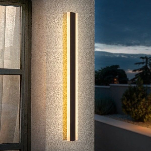Vertikal fasadlampa med varmt, bländdämpat ljus vid ett fönster